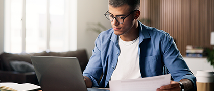Homem utiliza notebook enquanto analisa documentos em ambiente de trabalho.