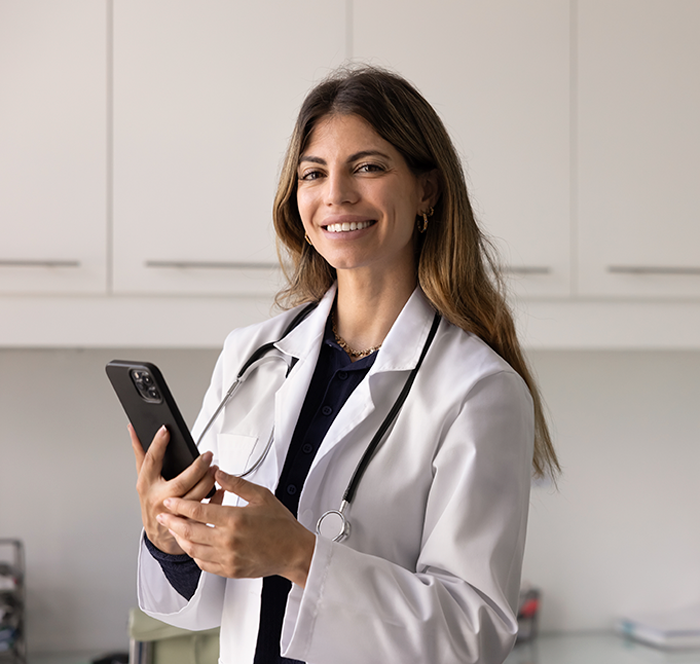 Profissional de saúde sorri enquanto utiliza o celular no consultório.