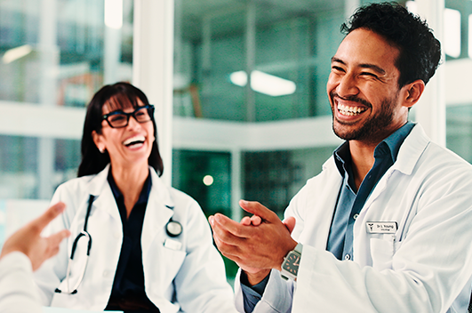 Médicos sorrindo durante reunião em ambiente hospitalar.